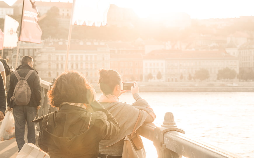 Woman taking photo of cityscape from bridge at sunset