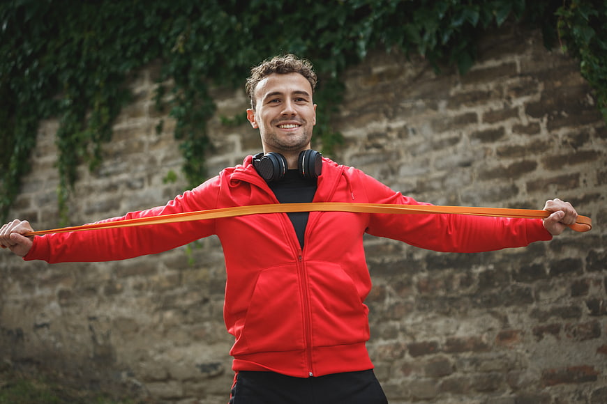 Happy Man Exercising with Resistance Band Outdoors