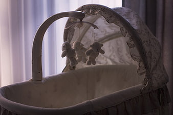 Empty white baby bassinet with mobile and stuffed animals