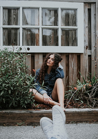 Woman in Denim Sitting by Wooden Fence with Window