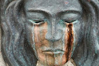 Close-up of weathered bronze sculpture face with closed eyes