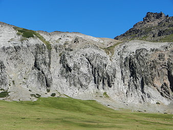 Rugged Mountain Cliff Face with Green Pasture and Blue Sky