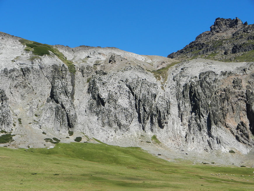 Rugged Mountain Cliff Face with Green Pasture and Blue Sky