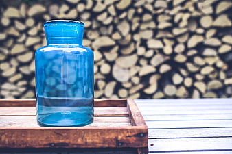 Blue glass jar on wooden tray with firewood background