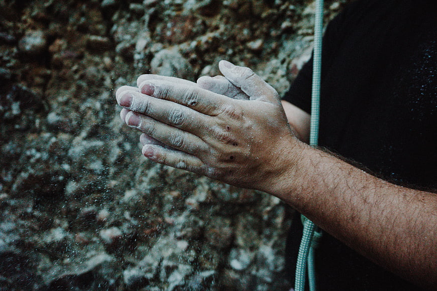 Rock climber chalking hands against textured rock wall