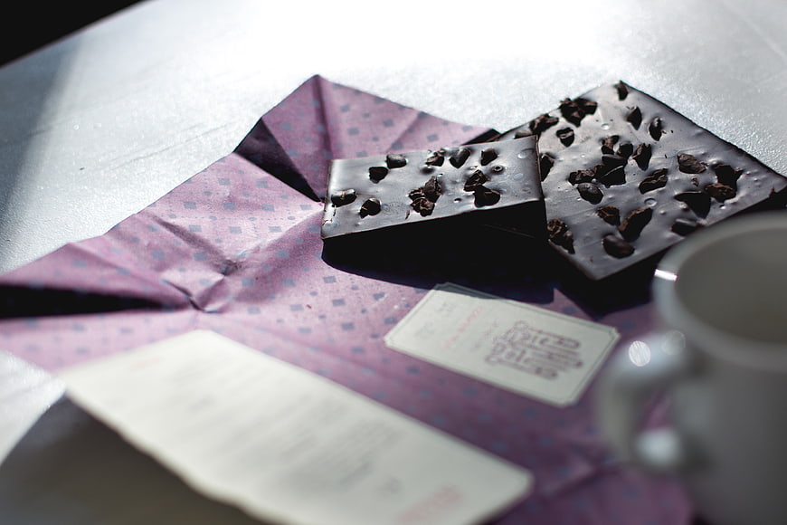 Dark chocolate pieces on purple paper with coffee cup