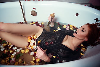 Woman in black dress relaxing in a bathtub with rose petals