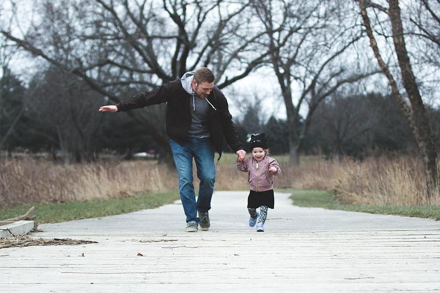 Father and Toddler Running Hand in Hand on Park Path