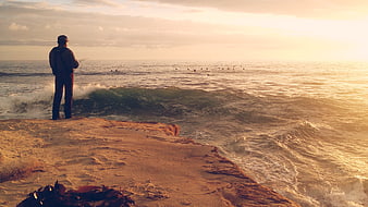 Man fishing from rocky cliff at golden sunset
