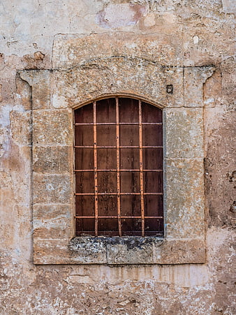 Old Arched Window with Iron Bars on Weathered Stone Wall
