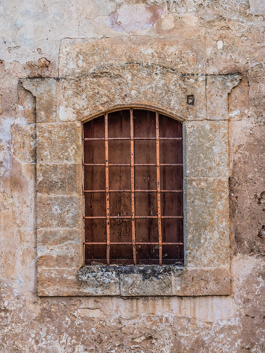 Old Arched Window with Iron Bars on Weathered Stone Wall