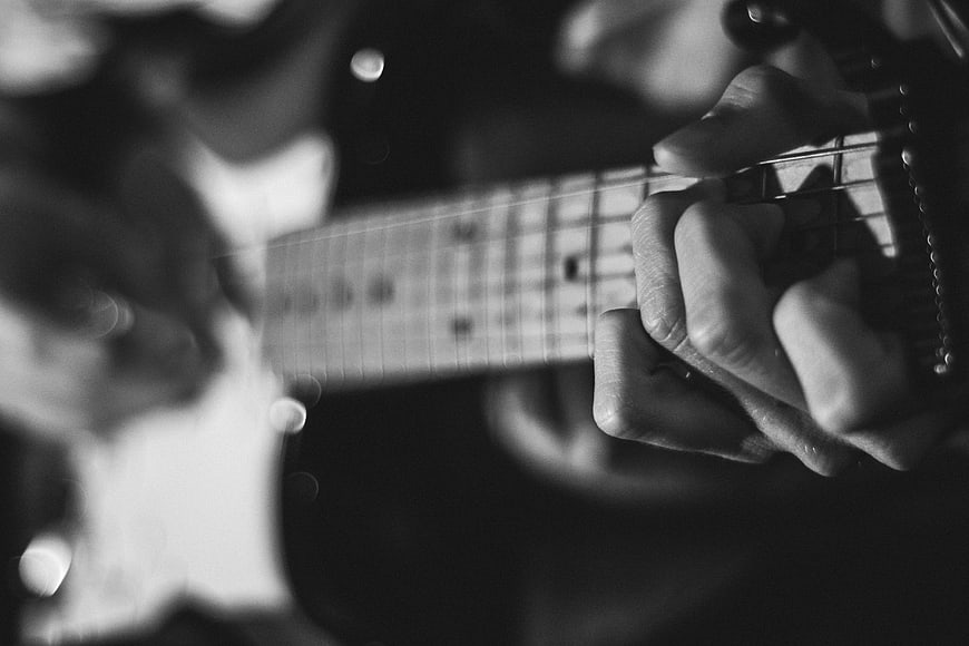 Close-up of hands playing electric guitar in black and white