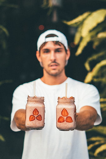 Man holding two strawberry smoothies in mason jars