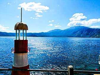 Red and white lighthouse on a boat deck overlooking blue lake and mountains