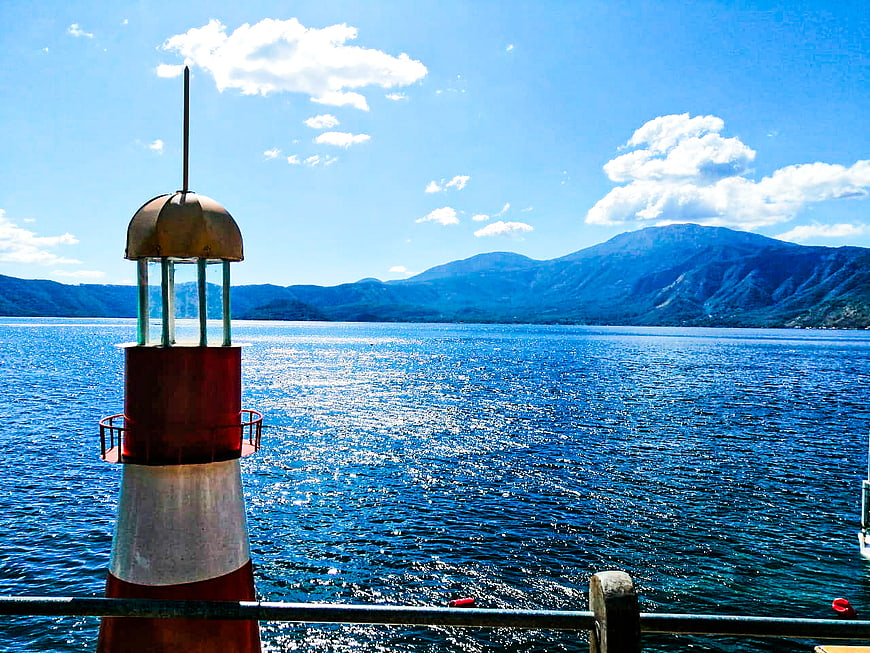 Red and white lighthouse on a boat deck overlooking blue lake and mountains