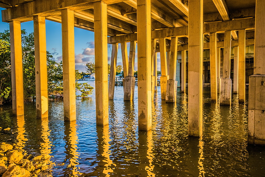 Sunlit concrete bridge pillars reflecting in calm water
