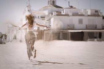 Woman Running Barefoot on Sandy Beach with White Buildings