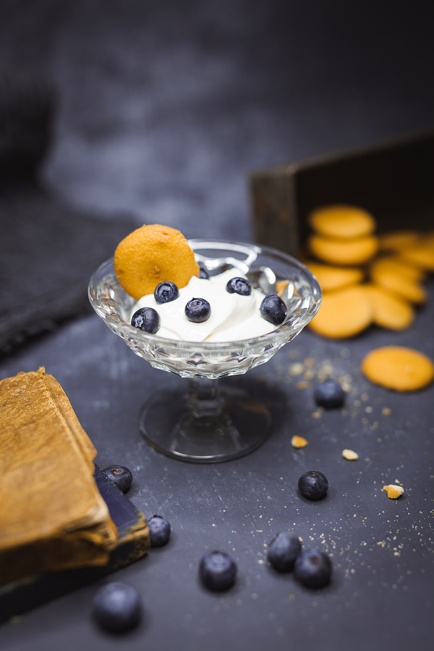 Cream dessert with blueberries and biscuit in glass bowl