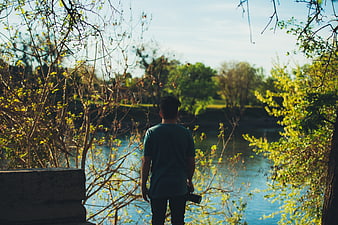 Man with Camera Looking at River Through Trees