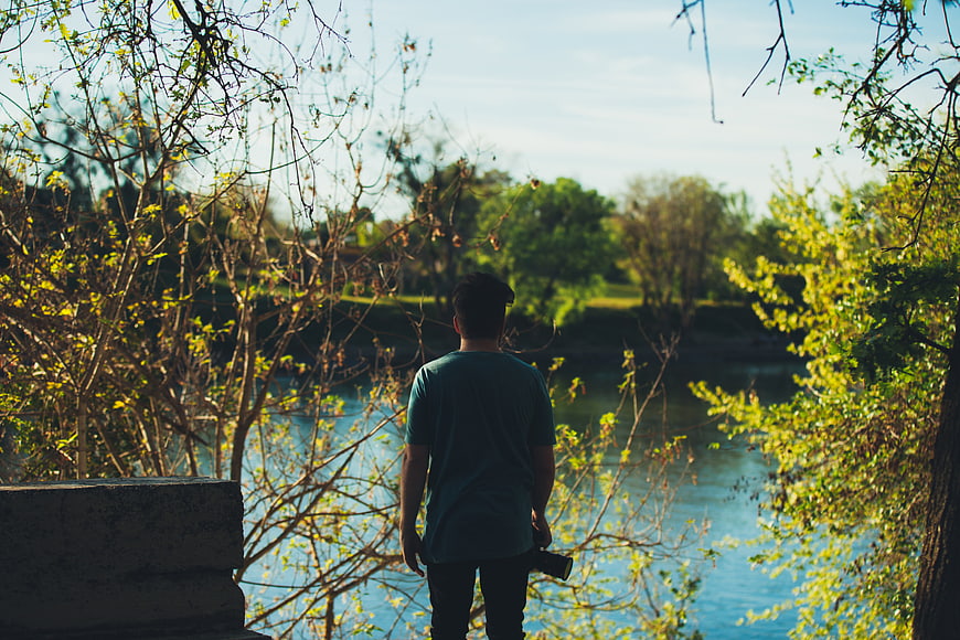 Man with Camera Looking at River Through Trees