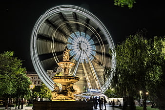 Illuminated Ferris Wheel And Ornate Fountain In Budapest Park At Night