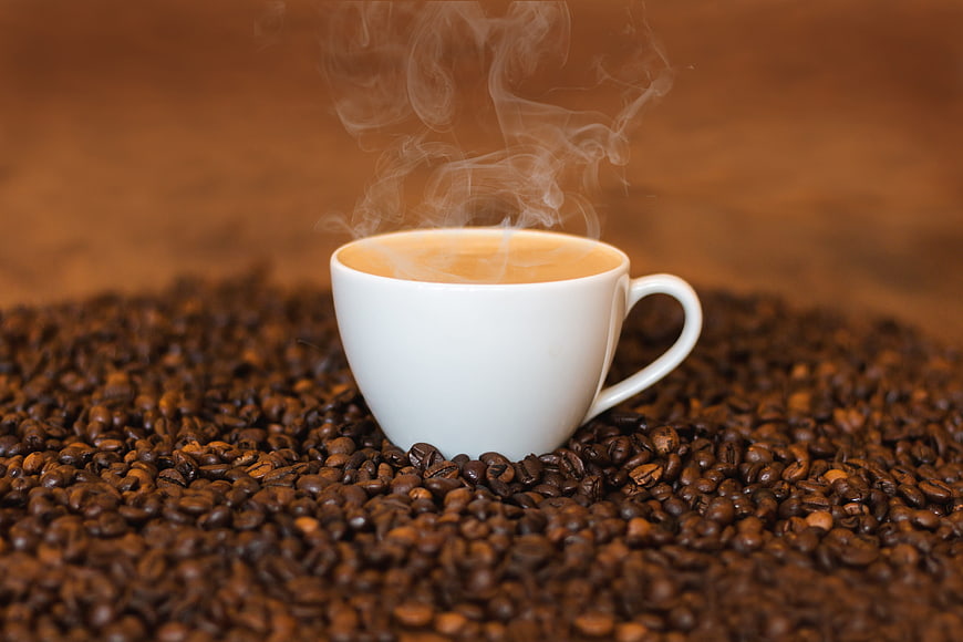 Steaming White Coffee Cup Surrounded by Roasted Coffee Beans