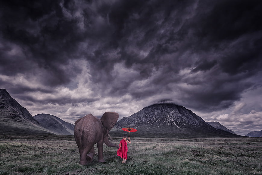 Child in Red Robe Walking with Elephant in Dramatic Mountain Landscape