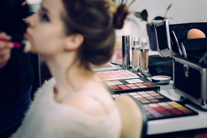 Woman Getting Makeup Applied with Cosmetics on Table