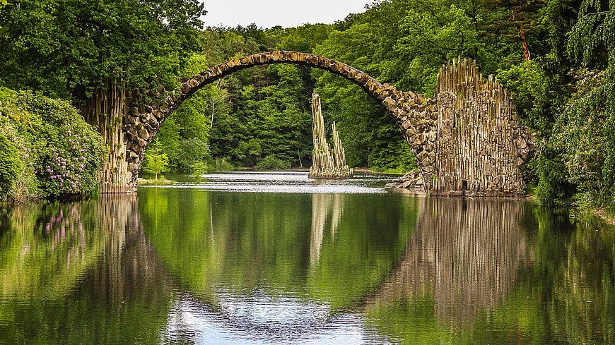 Stone Arch Bridge Over Calm River in Lush Green Forest