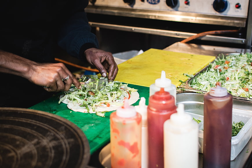 Street food vendor preparing fresh wraps with condiments