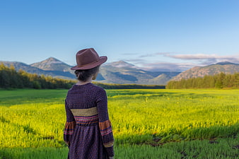 Woman in Hat Looking at Mountain Landscape from Green Field