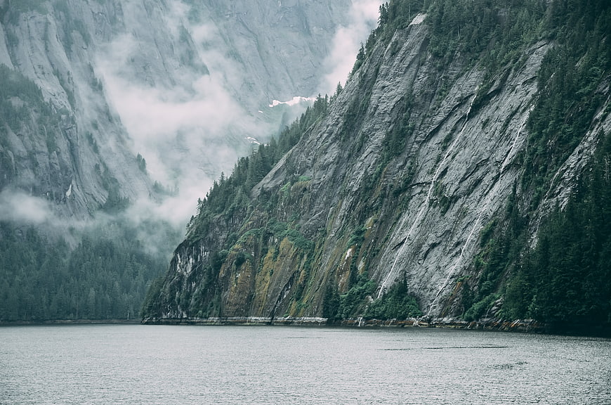 Misty mountain lake with steep cliffs and evergreen forest