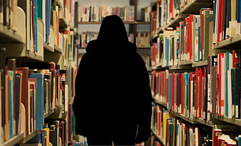 Silhouette of person walking through library bookshelves