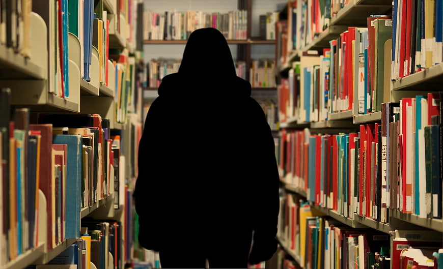Silhouette of person walking through library bookshelves