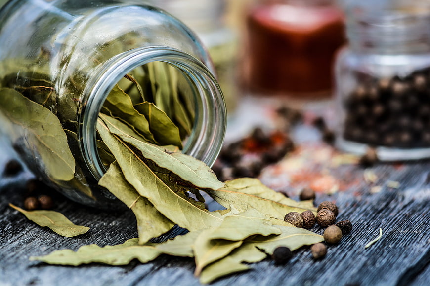 Dried Bay Leaves Spilling from Glass Jar on Rustic Wood