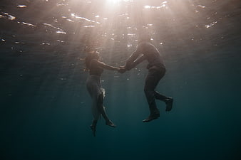 Romantic couple holding hands underwater in ocean sunlight