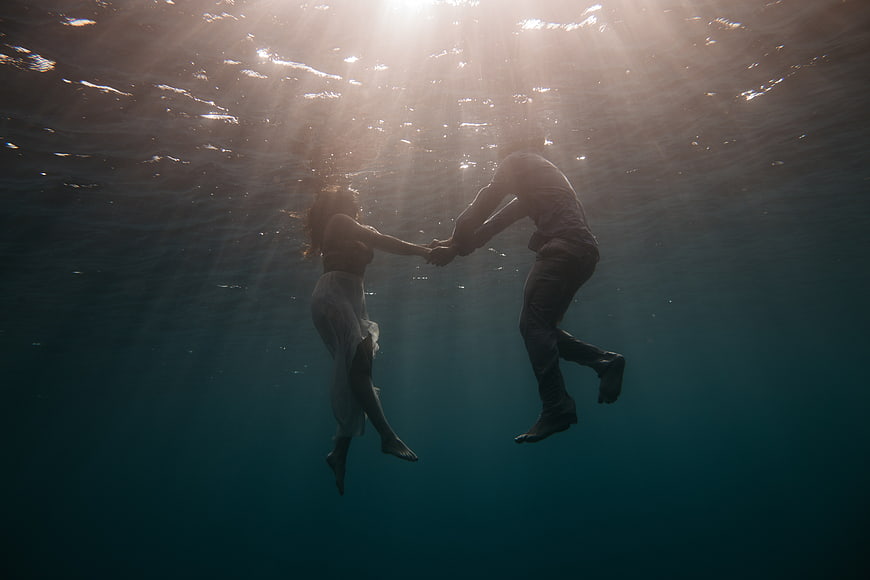 Romantic couple holding hands underwater in ocean sunlight