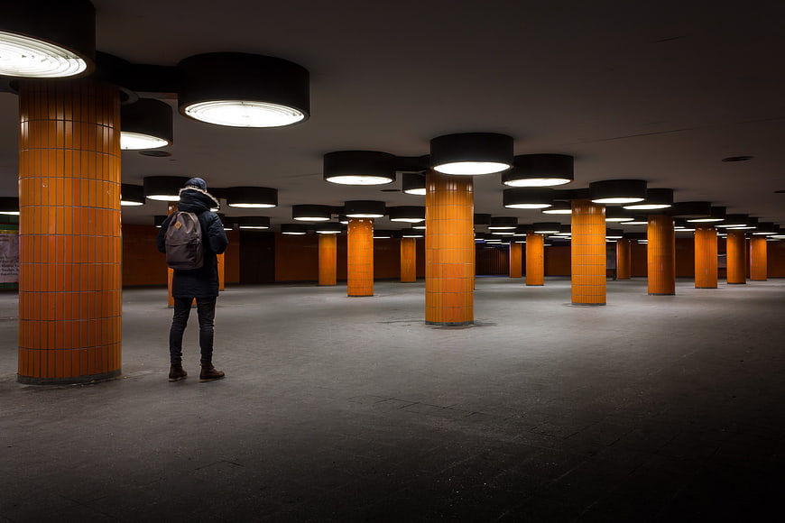 Man standing alone in large underground parking garage with orange tiled pillars