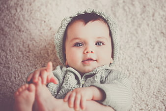 Adorable Baby in Gray Knit Hoodie Lying on Carpet
