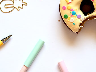 Flat lay of donut with sprinkles and pastel stationery on white background