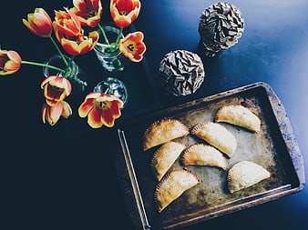 Flat lay of baked empanadas on tray with tulips