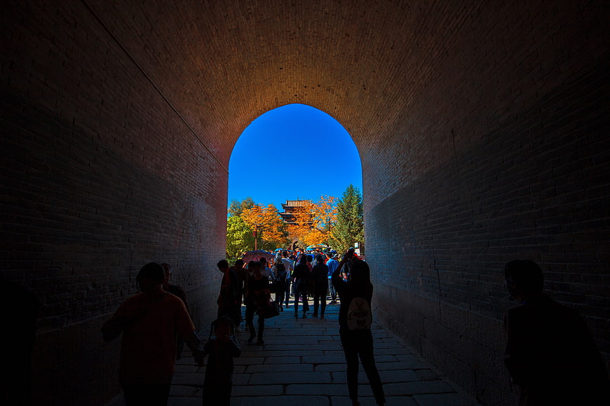 Tourists walking through ancient brick archway to autumn scenery