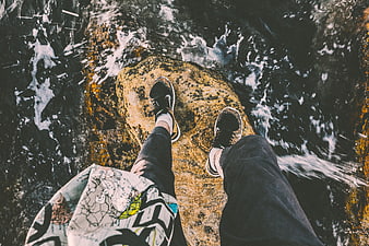 First-person view of sneakers on a rock by rushing water