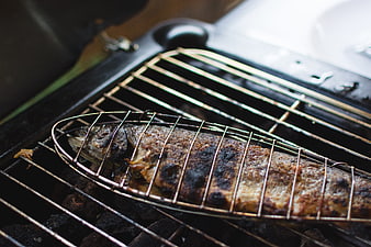 Whole grilled fish cooking in wire basket on charcoal barbecue