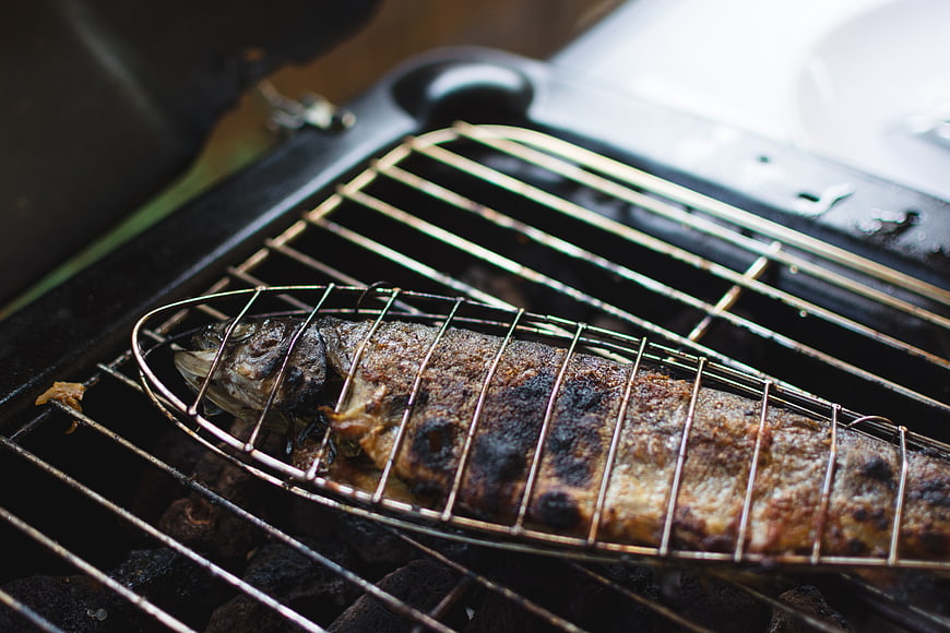 Whole grilled fish cooking in wire basket on charcoal barbecue