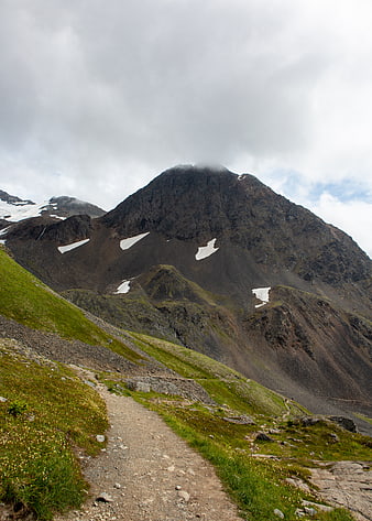 Mountain hiking trail with snow patches and cloudy sky
