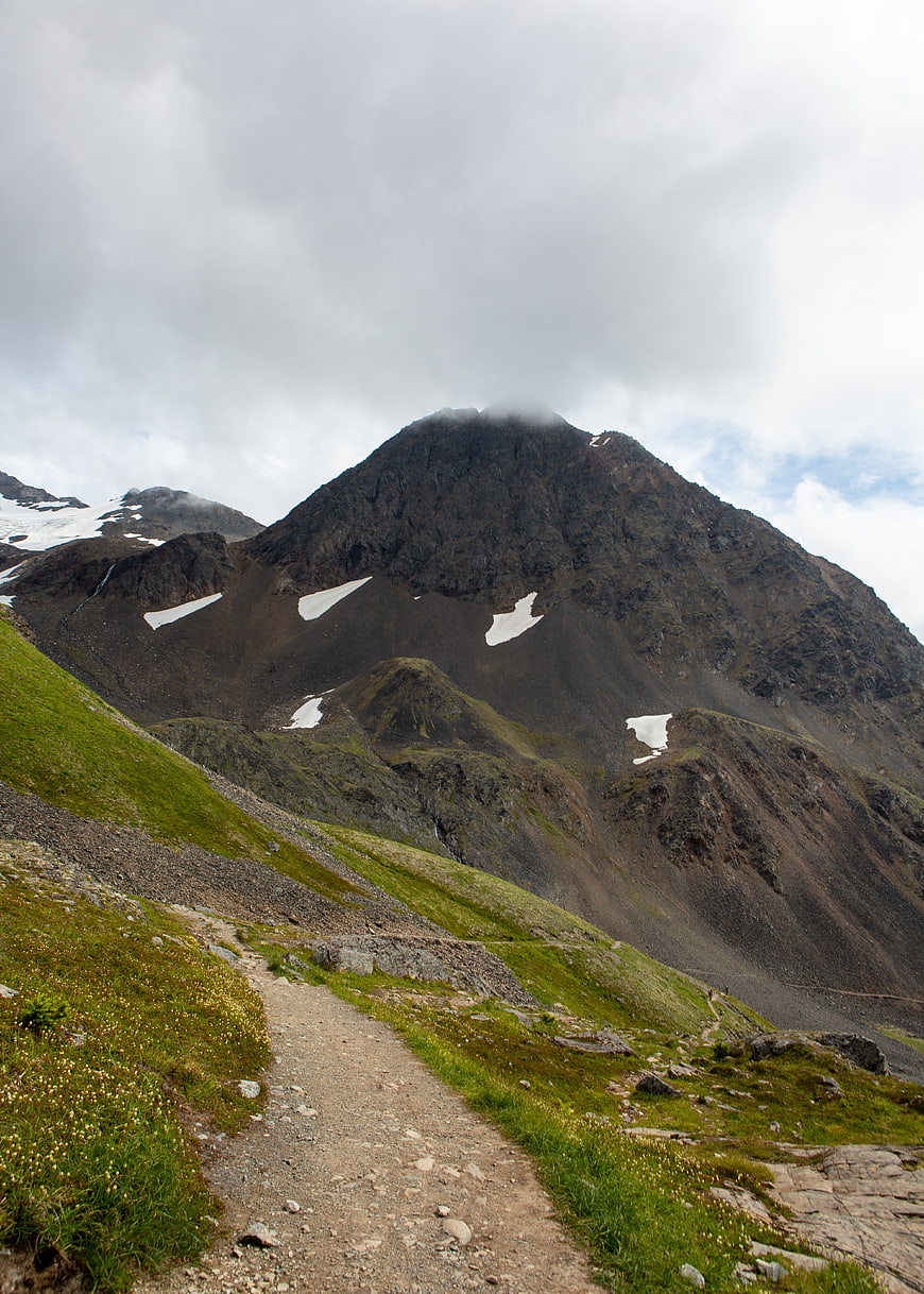 Mountain hiking trail with snow patches and cloudy sky