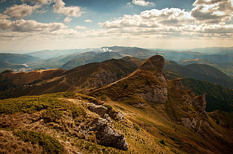 Hiker on rocky mountain peak with dramatic clouds and sun rays