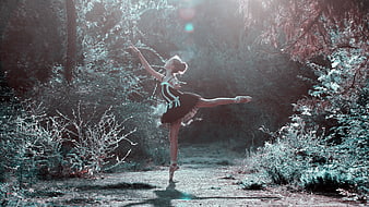 Ballerina performing arabesque in sunlit forest path