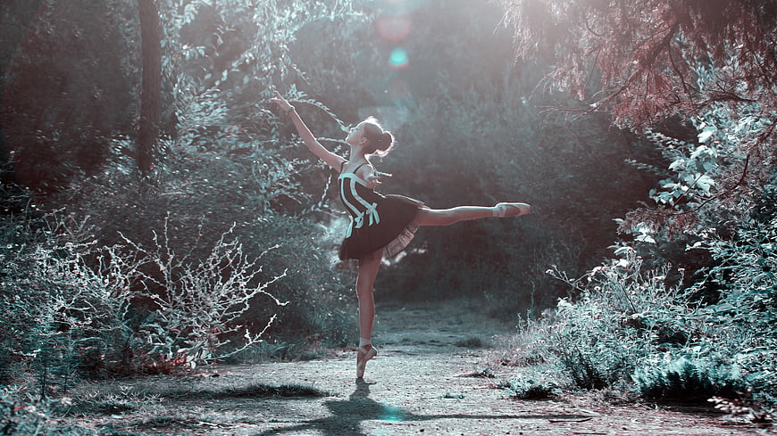 Ballerina performing arabesque in sunlit forest path